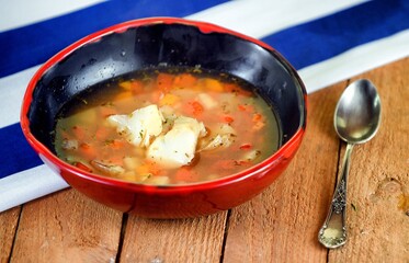 Red, fish soup with chilli papper, carrot, fish parsley and pore in a red and black bowl on wooden...