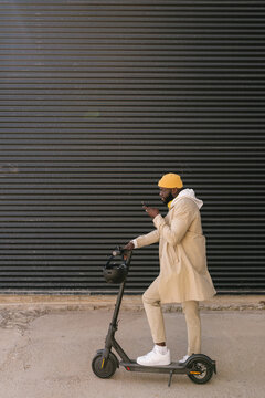 Black man recording a voice message with a mobile standing on an electronic scooter.