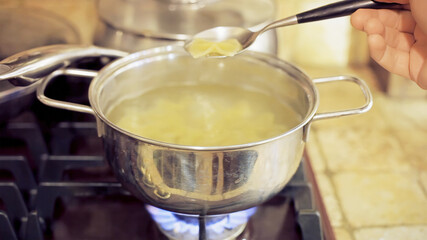 Italian pasta, farfalle, cooking in a pot full of boiling water; picking one with a spoon to check it.
