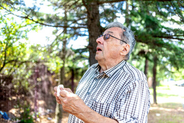 Fototapeta premium Portrait of modern senior man wearing eyeglasses allergic to the pollen blowing his nose on a summer day. Shot of an old man blowing his nose outdoors. Cropped shot of a man suffering with allergies.
