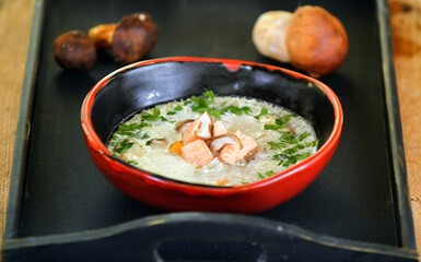 Cream soup with mushrooms, parsley and salmon in a red and black bowl on wooden background.