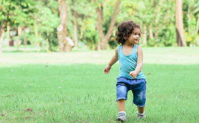 Little Caucasian little cute adorable curly hair playful girl wearing casual clothes, running alone with happiness and amusement in green garden or park or backyard during holidays.