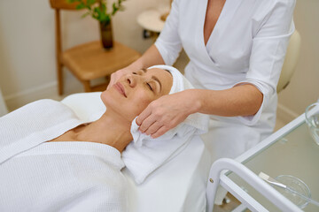 Cosmetologist doing face massage adult woman patient in beauty salon