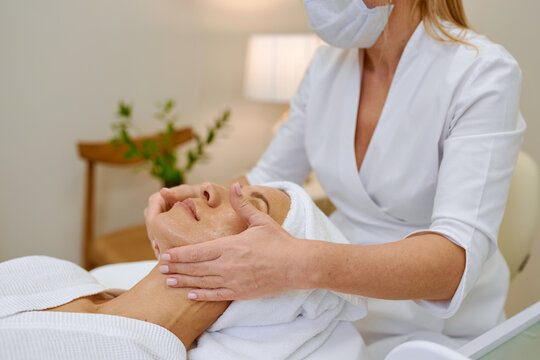 Cosmetologist doing face massage adult woman patient in beauty salon