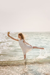 Portrait of beautiful little girl is playing with seashell in sea waves. Kid and vacation, tourist destination. Ballet dancer.