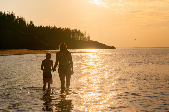Mother and Son Walking Along Red Sand Beach Seashore on PEI at Sunset