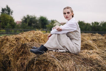 Naklejka na ściany i meble beautiful young woman in a light dress on a haystack. Agriculture.