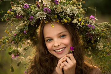 Cute smiling little girl with flower wreath on the meadow at the farm. Portrait of adorable small...