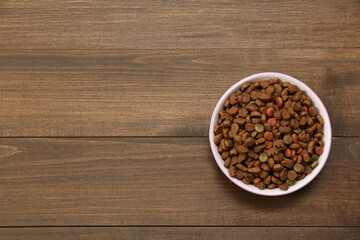 Dry food in pet bowl on wooden background, top view. Space for text
