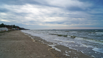 Black sea with waves and white foam under the blue sky in the clouds on a spring cloudy day