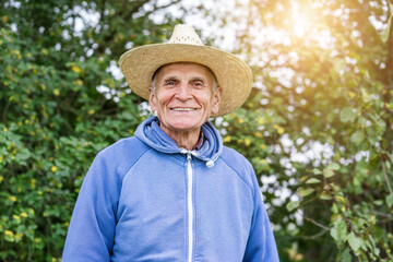 Elderly positive farmer wearing big straw hat standing on farm yard outdoor