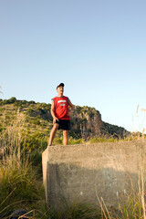 Mustached man with shorts and hat looking at the panorama on a concrete block on a hill. 