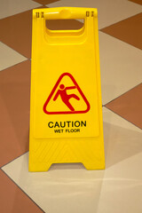 Yellow sign with the words Caution Wet Floor on tiled floor. The concept of cleaning, cleaning service, hotel, security measures. Sign showing warning of caution wet floor ..