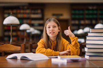 happy teenage girl in casual clothes sits at a table with books