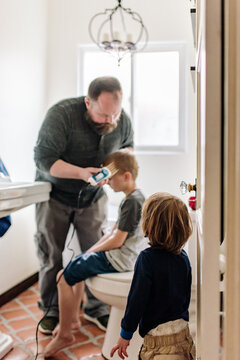 Young boy watching as his father clips his brother's hair at home