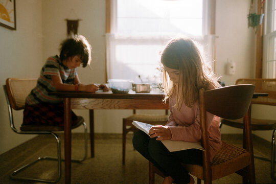 children sit at kitchen table reading books and doing homework