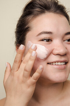Beautiful east asian woman applying pink cream on her face smiling

