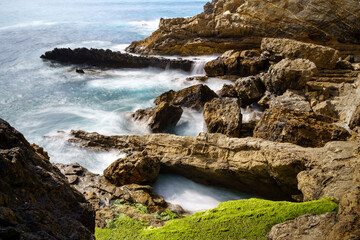 Waves crashing against cliff rocks in long exposure photography. Santander.