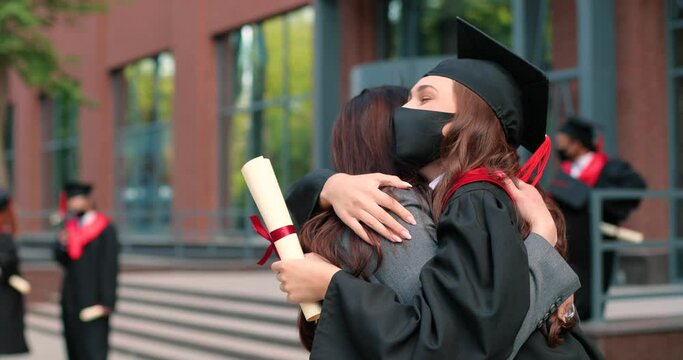 My smart daughter. Waist up portrait view of the happy brunette student woman wearing protective mask holding her diploma and embracing with her mother after her graduation