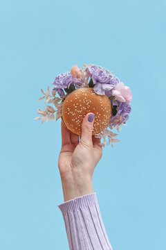Woman holding burger with flowers on blue background