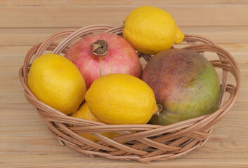 Mango lemon and pomegranate in a basket - fruit health benefits concept - wooden background