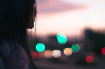 side view of an asian long haired woman on the street looking at sunset. blurred bokeh background.