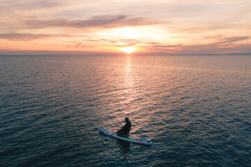 Fototapeta premium silhouette of a surfer in open water looking at the sun during a colorful sunset