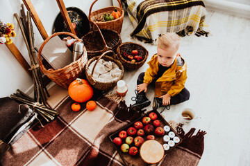 Cool trendy hipster boy 2 years old wears yellow jacket posing at the decorated photozone of autumn decor with beautiful bright autumn leaves.