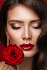Fototapeta na wymiar Woman Red Lips with Rose Flower. Beauty Model Face Makeup with Closed Eyes. Fashion Brunette Girl Close up Portrait over Red Background