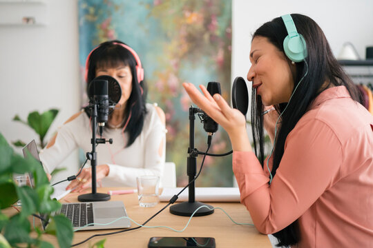 Cheerful female blogger speaking to microphone in studio with guest