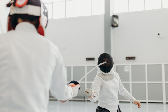 Female fencers in protective uniform dueling during training in gym