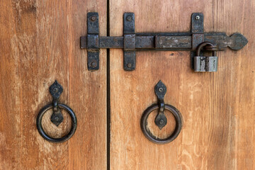 Close-up of wooden doors with wrought iron handles and a deadbolt.