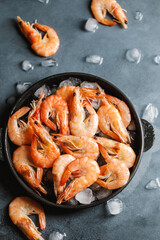 Raw shrimps with ice cubes on grey background. Uncooked shrimps