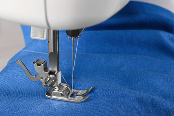 Modern sewing machine with blue cloth, closeup
