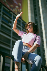 Portrait of a girl with curly hair dressed casually sitting outdoors and looking towards sun.