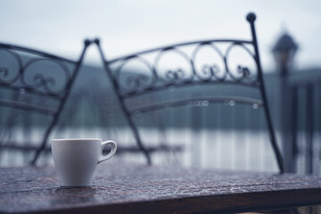 white cup of espresso coffee on wooden table on rainy outdoor terrace