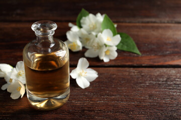 Essential oil and jasmine flowers on wooden table. Space for text