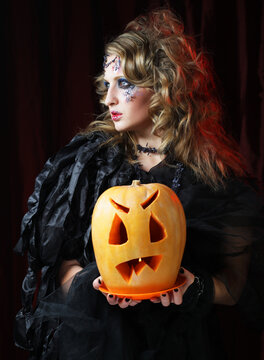 beautiful woman in a witch costume with bright makeup and hairstyle holding a pumpkin