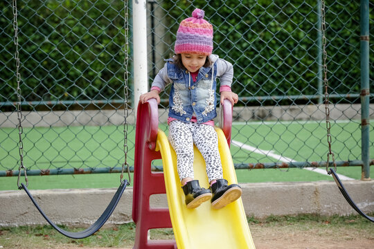 Crian&ccedil;a linda brincando num parquinho de touca rosa e blusa azul no inverno depois da quarentena do covid 19.