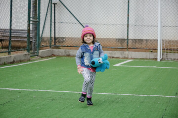 Criança linda brincando num parquinho de touca rosa e blusa azul no inverno depois da quarentena...