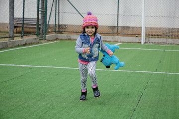 Criança linda brincando num parquinho de touca rosa e blusa azul no inverno depois da quarentena...