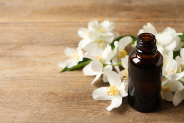 Jasmine essential oil and fresh flowers on wooden table, space for text