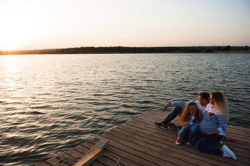 Fototapeta premium a pregnant mother, her husbant and daughter relaxing on the bridge by the river