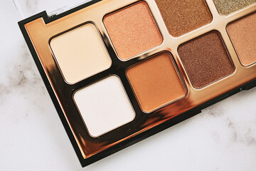 Colorful cosmetic eyeshadow palette makeup set with golden tint on marble background.