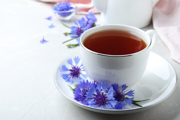 Obraz na płótnie Canvas Cup of tea and cornflowers on light table, closeup. Space for text