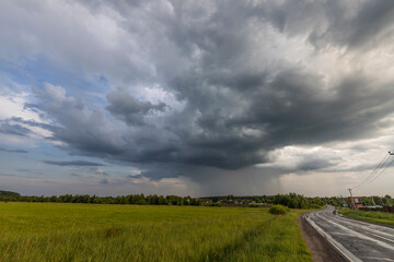 Rain clouds over the field. The road to the village. Green grass in the field. Summer landscape...
