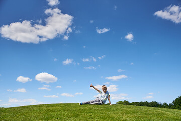 Boy 9 years old sits on a hill with green grass, summer