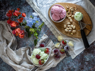 Bowl and scoops with delicious raspberry, cherry and pistachio ice cream.Wooden plate with delicious ice cream and different ingredients on the table decorated with branches and flowers.