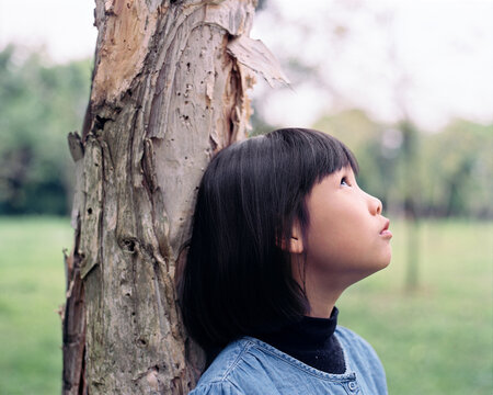 Cute Asian little girl leaning back against the tree, outdoor in the woods. Shooting 120 film camera