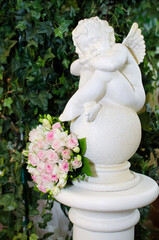sculpture of an  small angel made of white stone and a wedding bouquet of roses. Valentine's Day.
